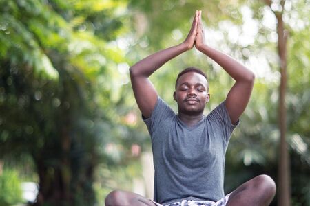 African man is meditating on green grass in the parkの写真素材