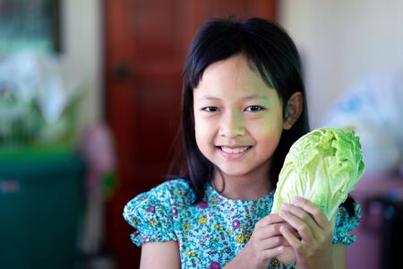 Smile asian child girl holding vegetables for cooking in the kitchenの写真素材