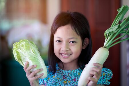 Smile asian child girl holding vegetables for cooking in the kitchenの写真素材