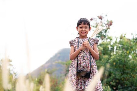 Asian little child girl holding film camera and taking photo with of green natural backgroundの写真素材