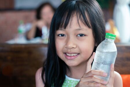 Asian children holding  and drinking cold water in restaurant. Healthy food and drink for Children conceptの写真素材