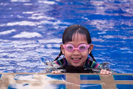 Cute little child girl with goggles in swimming poolの写真素材