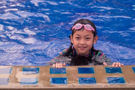 Cute little child girl with goggles in swimming poolの写真素材