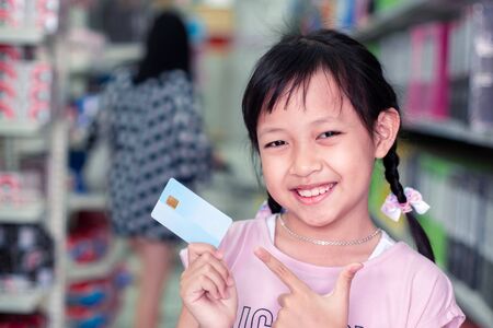 Smile child girl standing in super market with credit cardの写真素材