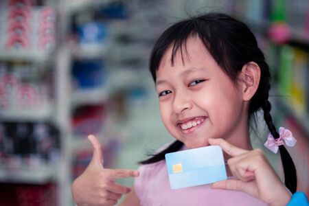 Smile child girl standing in super market with credit cardの写真素材
