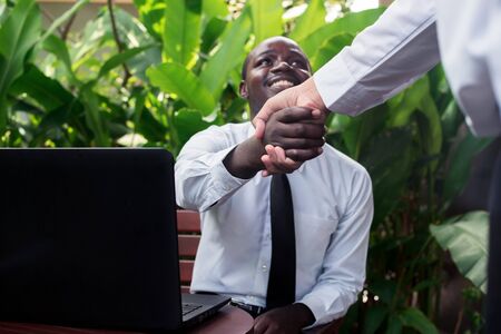 African business people shaking hands after contract signing at the coffee shop with laptop stand on the deskの写真素材