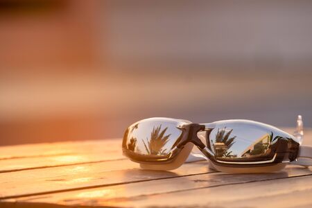 Swimming goggles on the wooden with the sunlight twilight