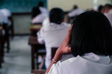 Students doing exam answer sheets exercises in classroom of school with stress.