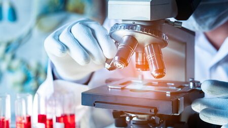 Scientist or doctor wear medical protective mask looking at blood samples under microscope.16:9 styleの写真素材