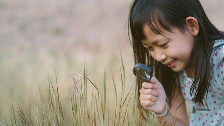 Happy asian child girl exploring nature with magnifying glass.16:9 styleの写真素材