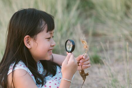 Happy asian child girl exploring nature with magnifying glass.