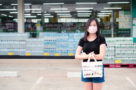 Asian woman shopping to a supermarket with a protective face mask and holding a basketの写真素材