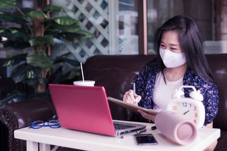 Woman working on laptop at home with wear medical face mask for protect for protect 2019 - nCov , covid 19 or corona virus.WFH or Working from home concept.の写真素材