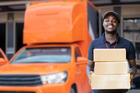 Smile african man postal delivery courier man in front of car delivering packageの写真素材