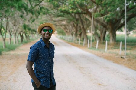 Portrait of the happy african man in sunglasses standing on the dirt road, smiling and looking at the camera.の写真素材