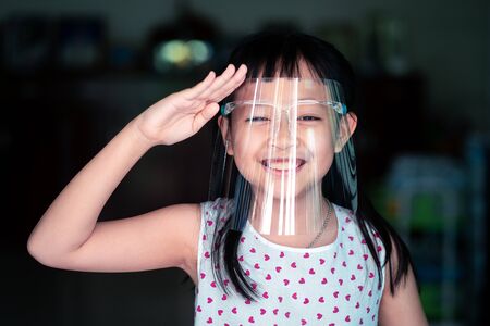 Happy little child girl with a plastic face shield for a virus protection mask on his faceの写真素材