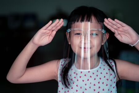 Happy little child girl with a plastic face shield for a virus protection mask on his faceの写真素材
