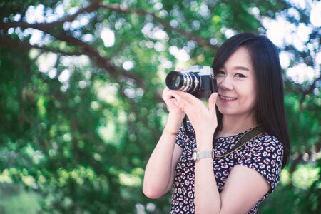 Portrait of beautiful smiling asian woman with holding camera at summer green park.の写真素材