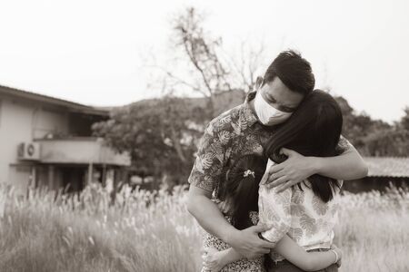 Father wearing face mask hugging his family standing back with love. Social distance stay at home during Covid-19 Pandemic concept.Black and white styleの写真素材