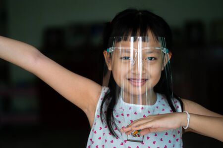 Happy little child girl with a plastic face shield for a virus protection mask on his faceの写真素材