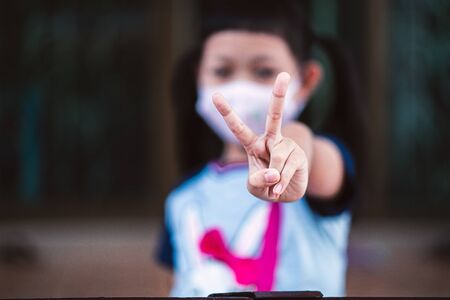Asian little child girl closeup raise two V shape finger wear a mask to safety Coronavirus to support in the fight against disease epidemic COVID 19 concept  at homeの写真素材