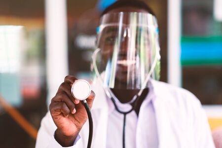 African doctor wear face shield and holding stethoscope with kind and smilingの写真素材