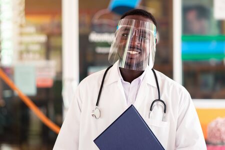 African doctor wear face shield and holding stethoscope with kind and smilingの写真素材