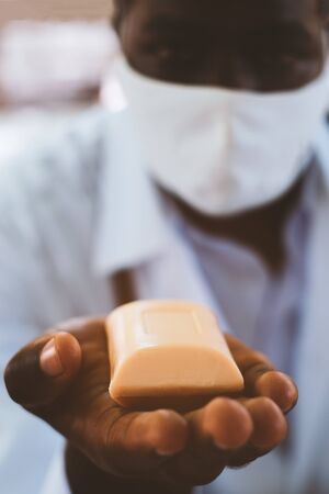 African doctor holds and show a piece of soap with wearing face maskの写真素材