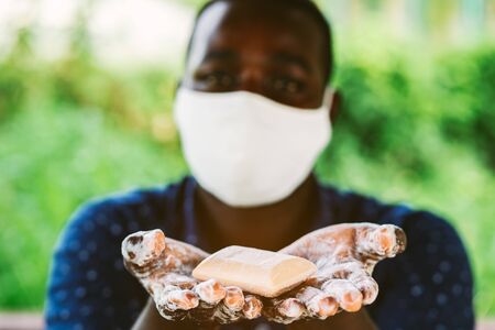 African man holds and show a piece of wet soap with wearing face maskの写真素材