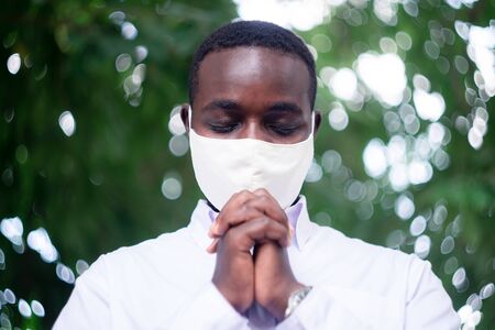 African man wear white shirt and face mask for virus protection with text Pray for the World corona virus covid-19 on green nature backgroundの写真素材