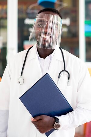 African doctor wear face shield and holding stethoscope with kind and smiling.の写真素材