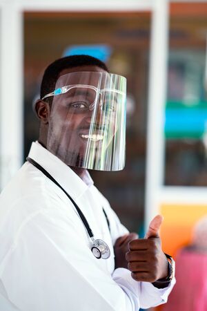 African doctor wear face shield and holding stethoscope with kind and smilingの写真素材