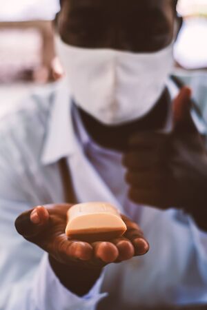 African doctor holds and show a piece of soap with wearing face maskの写真素材