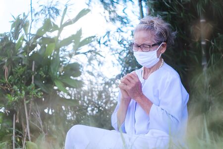 Old woman wearing mask and praying covid-19 or corona virus outbreak in parkの写真素材