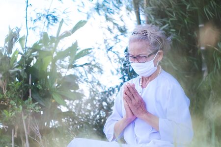 Old woman wearing mask and praying covid-19 or corona virus outbreak in parkの写真素材
