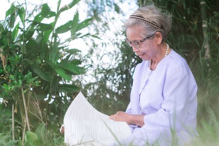Beautiful old woman reading book at parkの写真素材