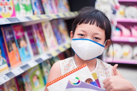 Asian little  child girl wear face mask and  buying school supplies in stationery store.Back to school conceptの写真素材