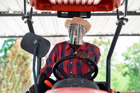 African farmer wear  face shield and driving tractor in farm during harvest in countryside....