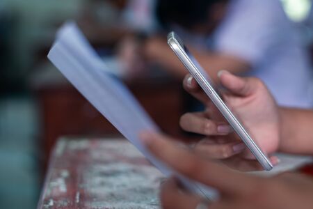 Students using smartphone and doing exam answer sheets exercises in classroom of school.16:9 styleの写真素材