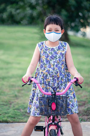 Little Asian girl wearing face mask and riding her bicycle outside with smile and happyの写真素材