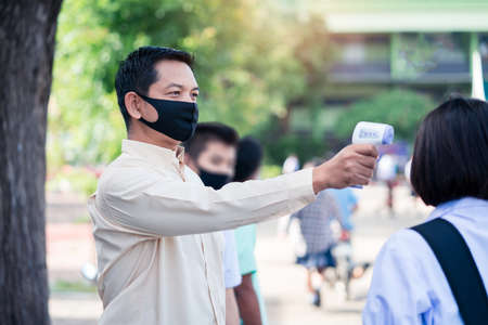 Teacher using thermometer temperature screening student for against the covid-19 or corona virus in the school.の写真素材