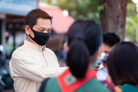 Teacher using thermometer temperature screening student for against the covid-19 or corona virus in the school.の写真素材