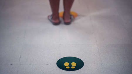 Stand here foot sign or symbol on the floor with the people is waiter , Social distancing concept.