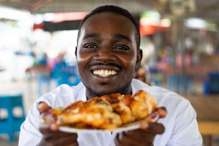 African man raising a grilled chicken on the dish with smile and happyの写真素材