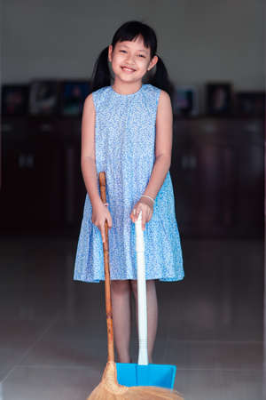 Smile asian little girl sweeping with broom and dustpan in the houseの写真素材