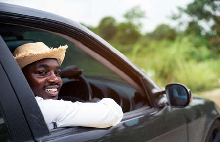 African man driver smiling while sitting in a car with open front windowの写真素材