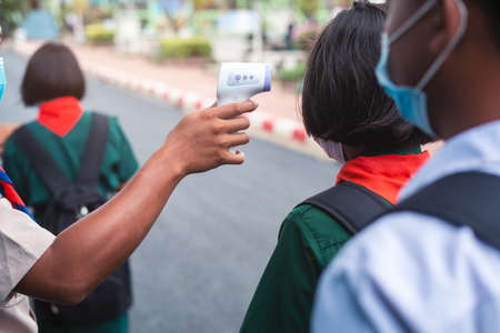 Hand holding Infrared thermometer gun forehead temperature test to check student for protect virus covid-19 symptoms in the schoolの写真素材