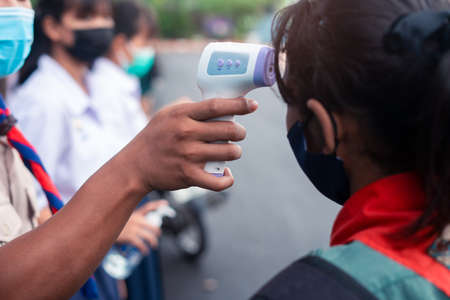 Hand holding Infrared thermometer gun forehead temperature test to check student for protect virus covid-19 symptoms in the schoolの写真素材