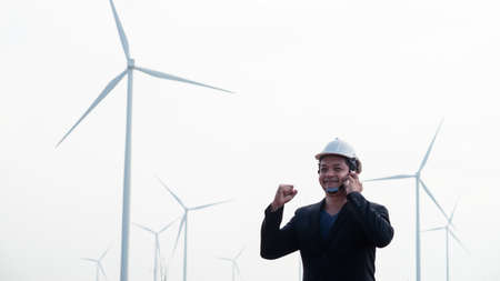 Successful asian engineer man standing and using smartphone with wind turbine.の写真素材