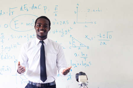 Science african teacher standing in front of blackboard teaching student in classroomの写真素材